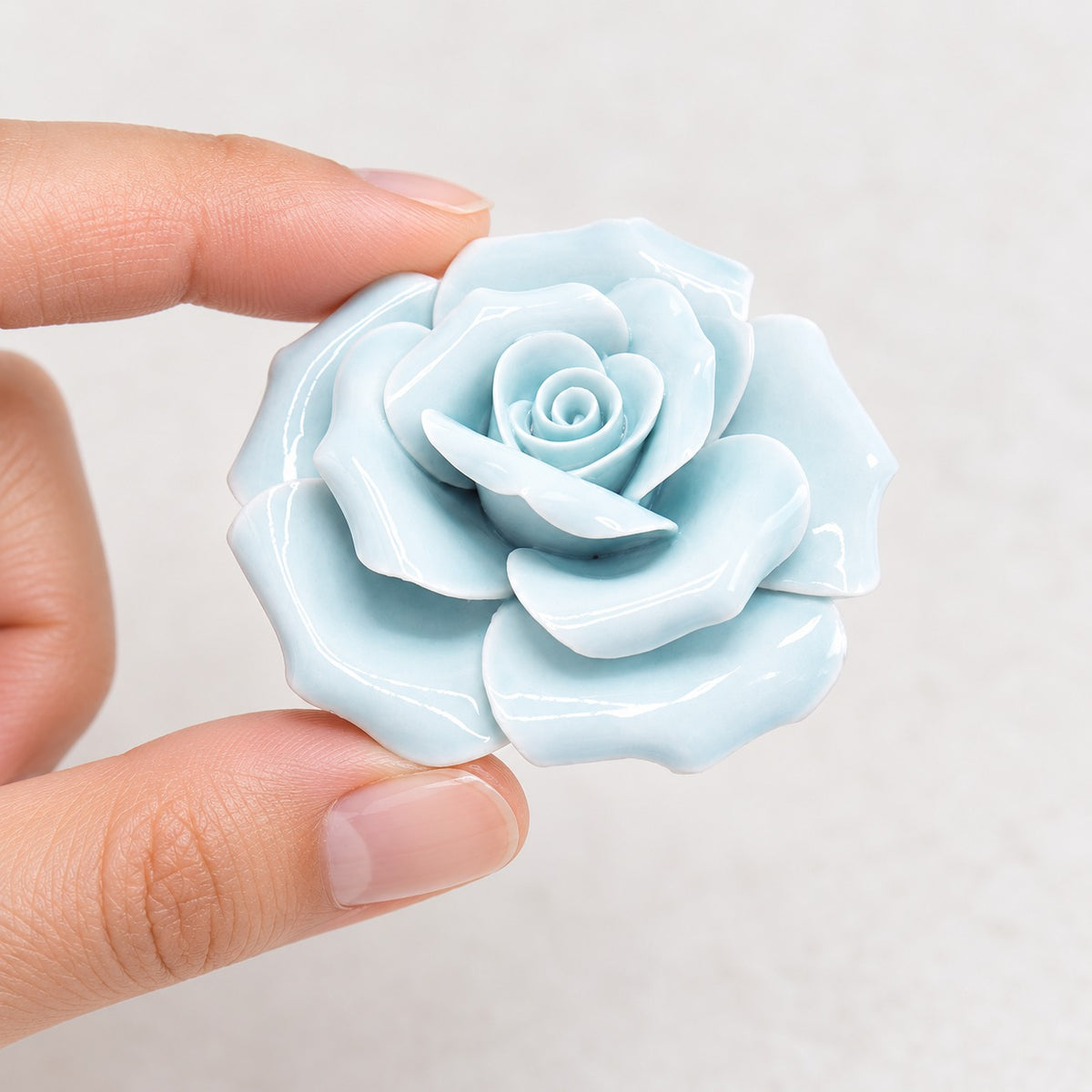Rosa in ceramica celeste 5,8 cm tenuta tra le dita per mostrarne le dimensioni